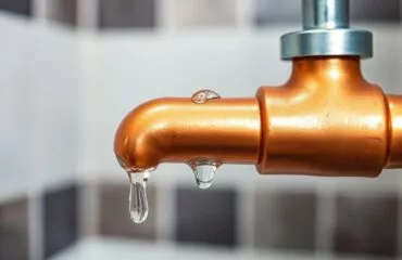 Close-up of a clean, shiny copper pipe section with subtle water droplets, highlighting plumbing maintenance plan benefits in a modern bathroom setting, ideal for Houston plumbing services.