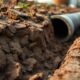 Ground level view of cracked clay soil with exposed pipe trench edge after rain highlighting cast iron sewer pipe problems, cast iron pipe repair Houston, and sewer line replacement Houston.