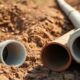 Close-up of clay and PVC sewer pipe sections placed side by side on bare earth, highlighting clay sewer pipes vs pvc for sewer pipe replacement houston.