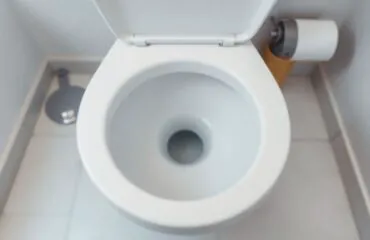 Clean white porcelain toilet bowl viewed from above in a bright modern bathroom, neutral tile floor, highlighting toilet bubbling and toilet gurgling issues for plumbing repair Houston.